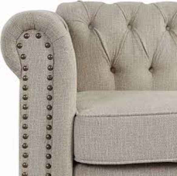 A warm beige mid-century modern accent chair with hand-pulled tufted buttons, silver-toned nailhead accents, and turned wooden legs. The chair features a plush, ergonomic design with foam cushioning and a tufted back for added texture and sophistication. The solid rubberwood frame and durable upholstery ensure long-lasting comfort and support, making it perfect for various rooms including the living room, office, or bedroom.