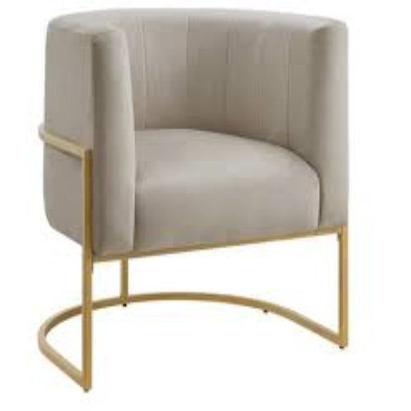 Taupe velvet barrel accent chair with gold accents and a hidden, storable ottoman. Features flared arms, foam-filled seat and back for comfort, a solid wood frame with a sled base for stability, and includes toss pillows for added comfort. The ottoman conveniently tucks under the chair to save space, creating a stylish, space-saving solution for any room.