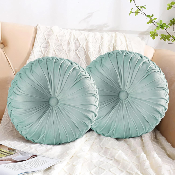 Aqua velvet round throw pillows with hand-sewn pleats and central button, set of two 14.5-inch decorative cushions styled on a modern sofa.