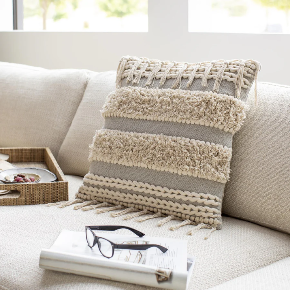 Beige and cream boho accent pillow with tassels and striped texture on a cozy neutral-toned sofa