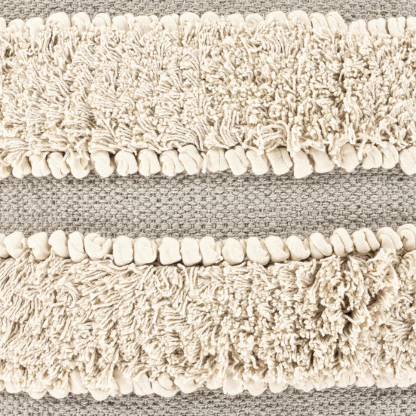 Beige and cream boho accent pillow with tassels and striped texture on a cozy neutral-toned sofa