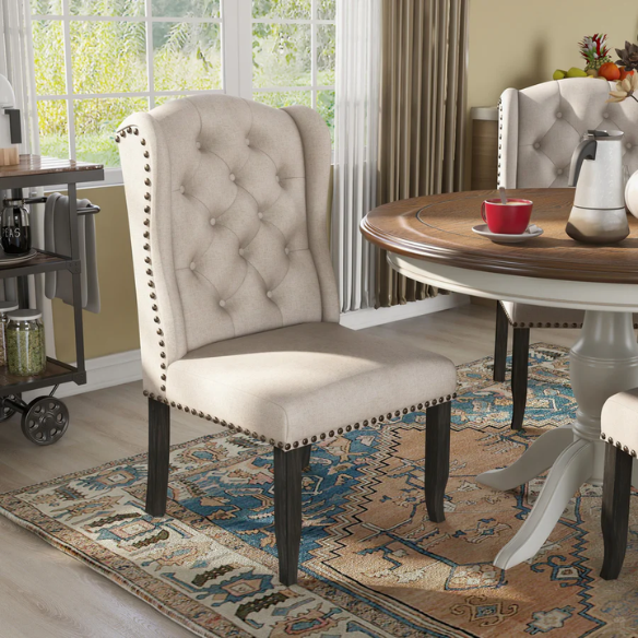 Set of two beige upholstered dining chairs with wingback design, button-tufted backrest, nailhead trim, and espresso-finished wooden legs