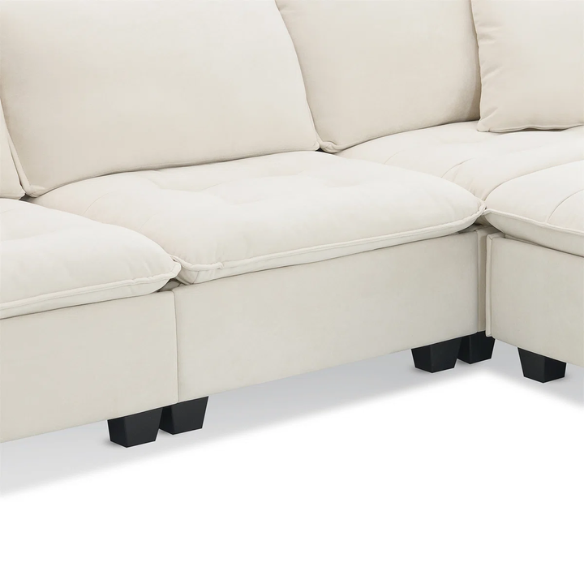 Beige suede L-shaped sectional sofa with removable ottoman, tufted seat cushions, and two matching accent pillows