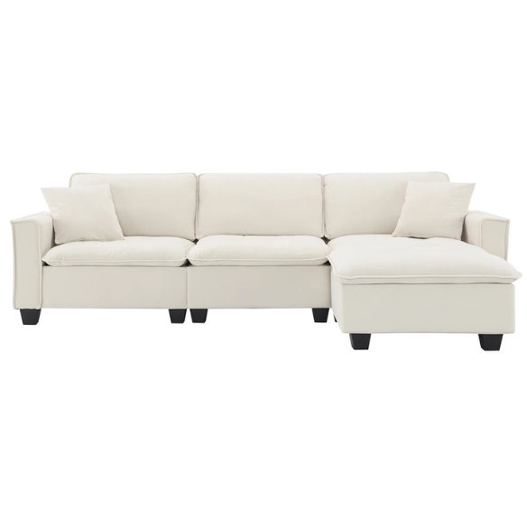 Beige suede L-shaped sectional sofa with removable ottoman, tufted seat cushions, and two matching accent pillows