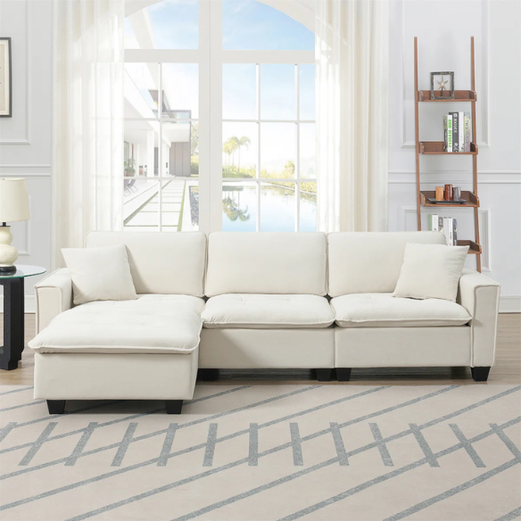 Beige suede L-shaped sectional sofa with removable ottoman, tufted seat cushions, and two matching accent pillows