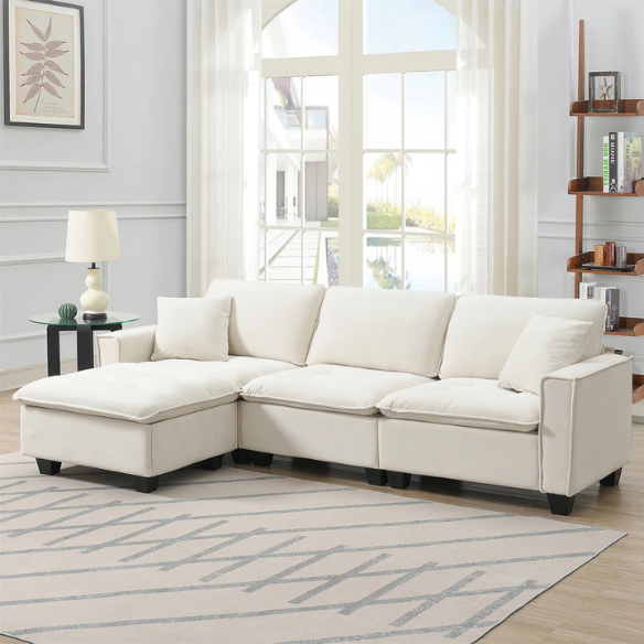 Beige suede L-shaped sectional sofa with removable ottoman, tufted seat cushions, and two matching accent pillows
