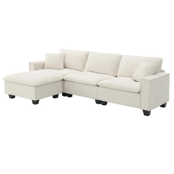 Beige suede L-shaped sectional sofa with removable ottoman, tufted seat cushions, and two matching accent pillows
