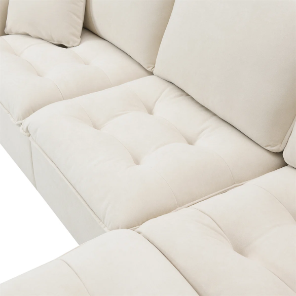 Beige suede L-shaped sectional sofa with removable ottoman, tufted seat cushions, and two matching accent pillows
