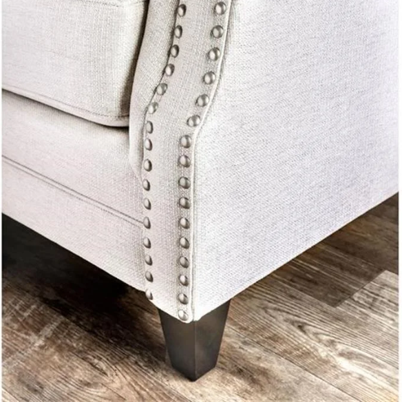 Beige tufted linen sofa with rolled arms, nailhead trim, tapered wooden legs, and accent pillows in transitional style.