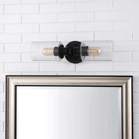 Art Deco-style black wall sconce with dual clear seeded glass cylinder shades and Edison-style LED bulbs, suitable for bathroom or hallway lighting