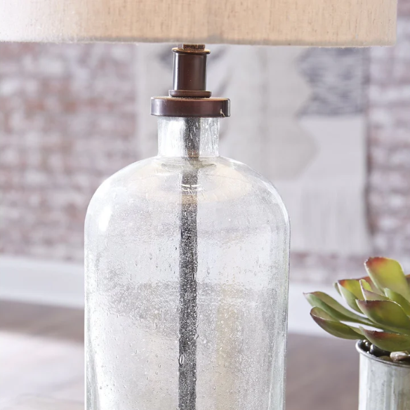 Bronze-tone seeded glass table lamp with beige fabric drum shade, featuring a metal base and compact design for modern farmhouse or industrial interiors