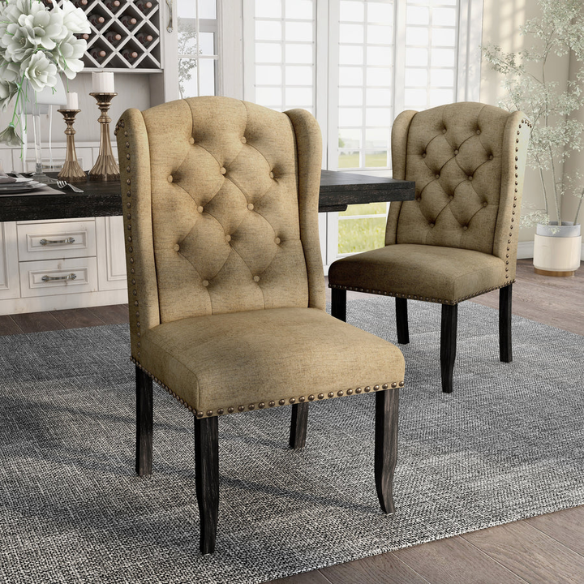 Set of two brown gold wingback dining chairs with tufted backs, nailhead trim, and espresso-finished legs, perfect for farmhouse or traditional dining spaces.