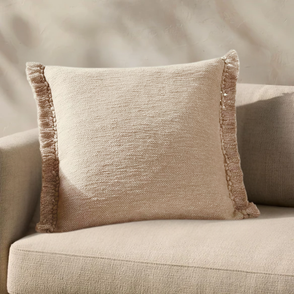 Cream cotton blend throw pillow with fringe, 22x22 square cushion, styled on a modern sofa for soft, neutral home decor.