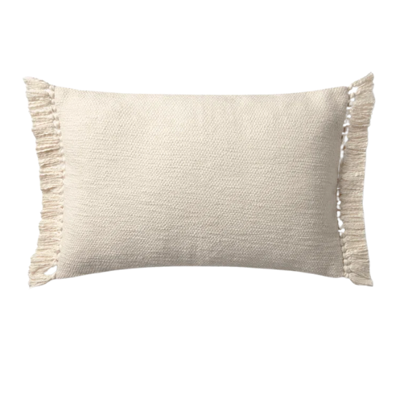 Cream lumbar throw pillow with soft fringe trim, rectangular 13x21 design, made from neutral cotton blend fabric, styled on a sofa for cozy, modern home decor.