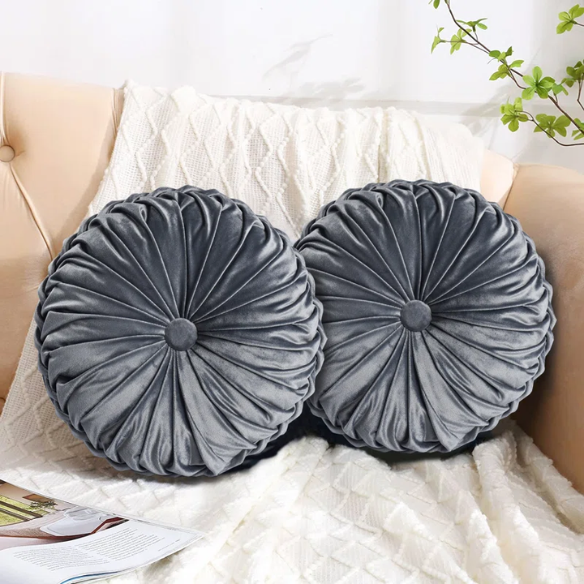 Dark grey velvet round throw pillows with hand-pleated design and button center, set of two 14.5-inch plush cushions styled in a modern living space.