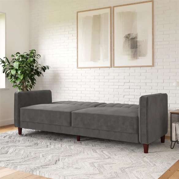Dark grey velvet convertible sofa with vertical tufting, split-back design, square arms, and brown tapered legs, convertible into a twin-size sleeper.