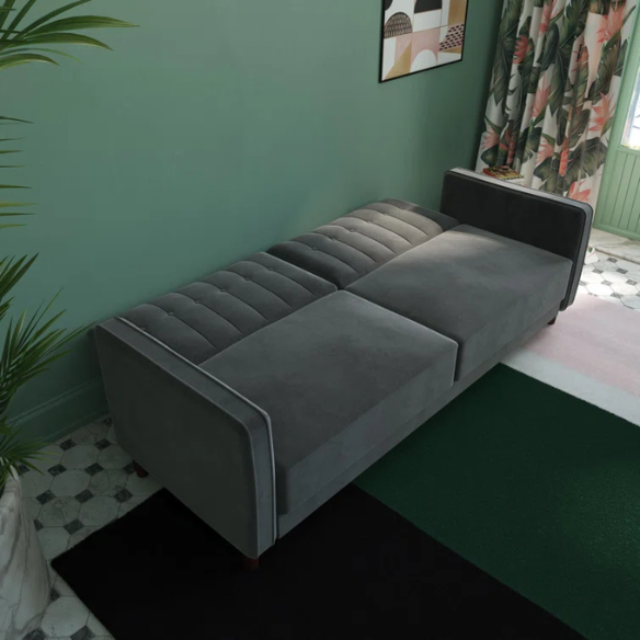 Dark grey velvet convertible sofa with vertical tufting, split-back design, square arms, and brown tapered legs, convertible into a twin-size sleeper.