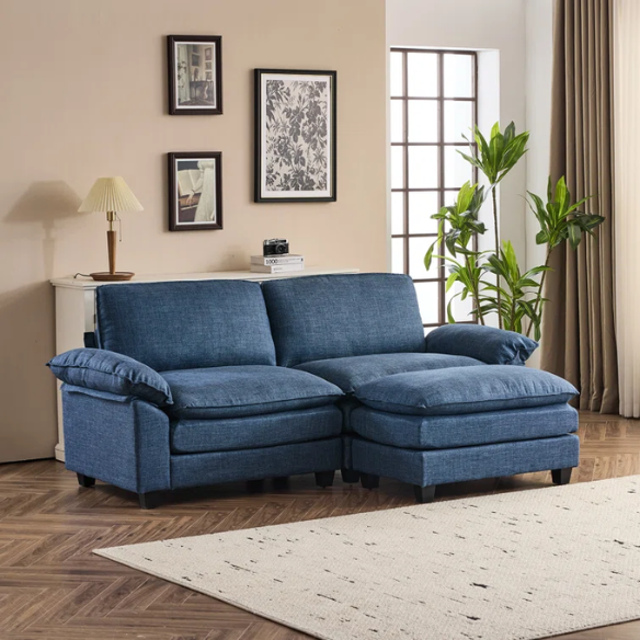Denim blue modular cloud sofa with deep cushioned seating, curved pillow arms, and free-standing ottoman