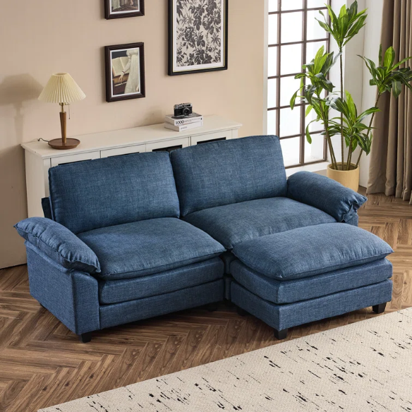 Denim blue modular cloud sofa with deep cushioned seating, curved pillow arms, and free-standing ottoman