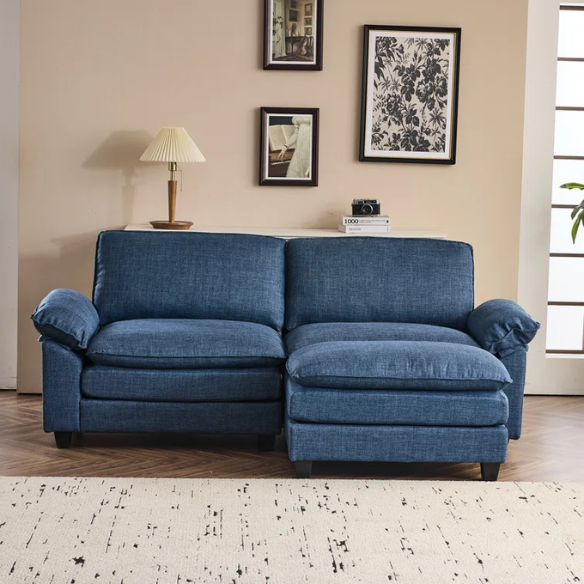 Denim blue modular cloud sofa with deep cushioned seating, curved pillow arms, and free-standing ottoman