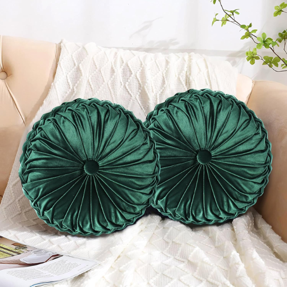 Emerald green velvet round throw pillows with hand-pleated detail and central button, 14.5-inch set of two on a white sofa in a stylish living room.