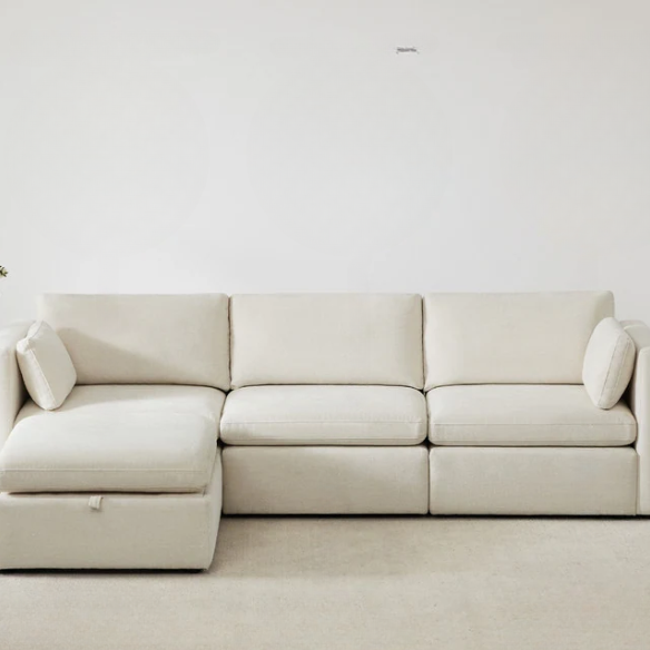Beige modular four-piece sectional sofa with wide seats, soft chenille fabric, removable cushions, and built-in storage ottoman — ideal for modern and adaptable living room layouts.
