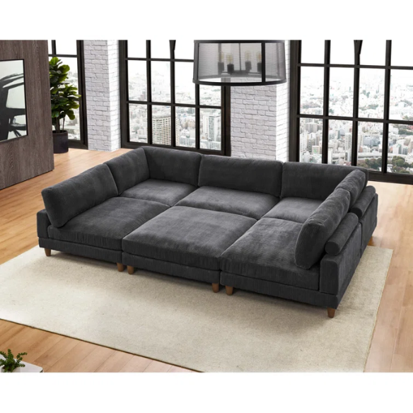 Dark grey modular sectional sofa with soft corduroy upholstery, matching ottoman, and removable cushions — seats six with flexible L- or U-shaped configurations.