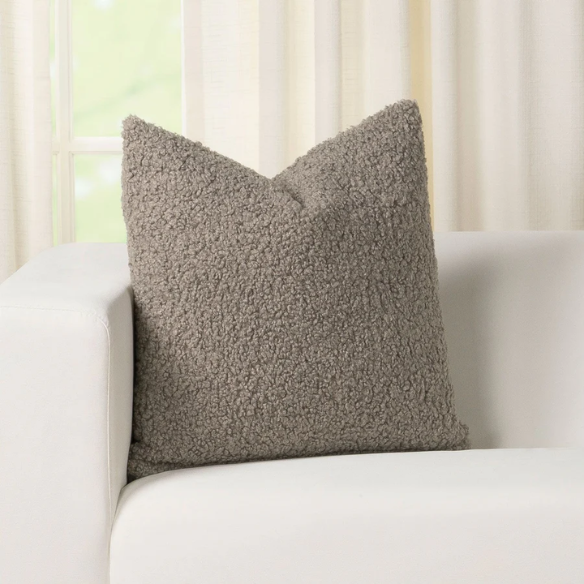 Grey bouclé throw pillow with soft looped texture, square accent pillow on a modern neutral-toned sofa
