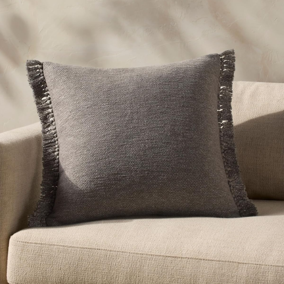 Grey cotton blend throw pillow with fringe, 22x22 square cushion featuring soft texture and hidden zipper, styled on a modern sofa for cozy, neutral decor.