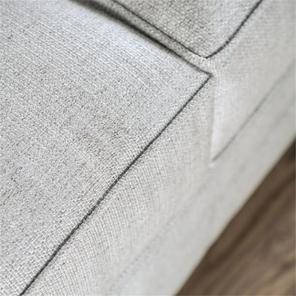 Grey tufted linen sofa with rolled arms, nailhead trim, tapered wooden legs, and accent pillows in a transitional design.