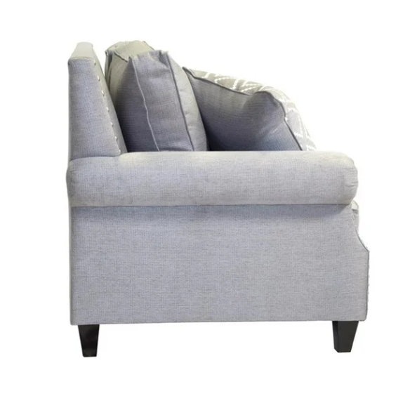 Grey tufted linen sofa with rolled arms, nailhead trim, tapered wooden legs, and accent pillows in a transitional design.