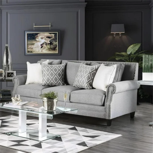 Grey tufted linen sofa with rolled arms, nailhead trim, tapered wooden legs, and accent pillows in a transitional design.