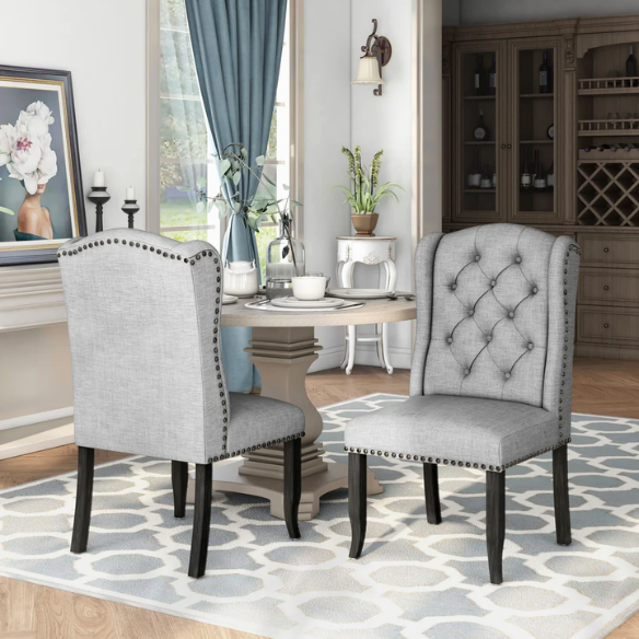 Set of two light grey farmhouse-style wingback dining chairs with button tufting, nailhead trim, and antique black tapered legs