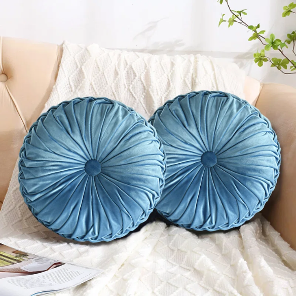 Muted blue velvet round throw pillows with pleated detailing and button center, 14.5-inch set of two styled on a neutral-toned sofa.