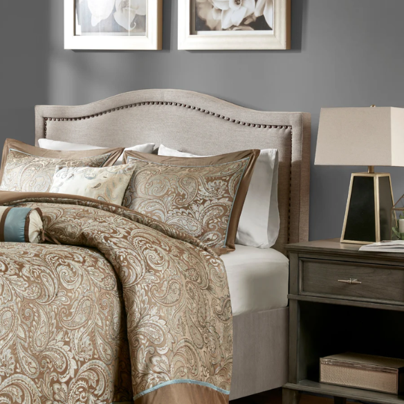 Natural beige upholstered king headboard with curved silhouette, silver nailhead trim, and adjustable metal legs for bed frame mounting