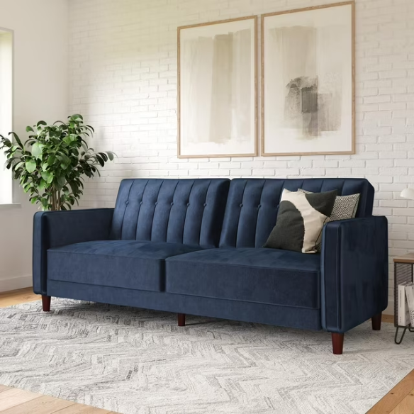 Navy blue velvet convertible sofa with vertical tufting, square arms, and brown tapered legs, designed with a split-back reclining feature and twin bed conversion.