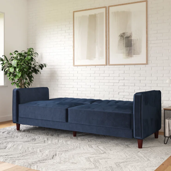 Navy blue velvet convertible sofa with vertical tufting, square arms, and brown tapered legs, designed with a split-back reclining feature and twin bed conversion.