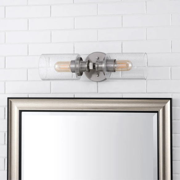Brushed nickel wall sconce with two clear seeded glass cylinder shades and Edison-style LED bulbs, perfect for bathrooms or hallway accent lighting