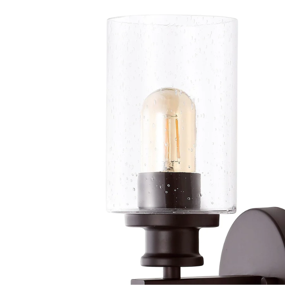 Oil-rubbed bronze wall sconce with dual clear seeded glass cylinder shades and Edison-style LED bulbs, perfect for rustic, farmhouse, or traditional interiors