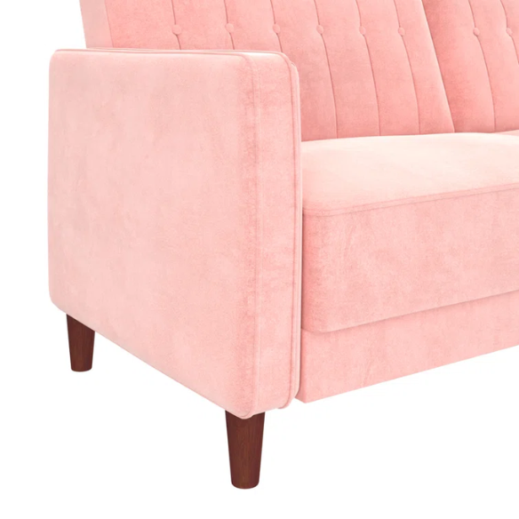 Pink velvet convertible sofa with tufted split-back design, square arms, and tapered brown wood legs, easily converting into a twin-size sleeper.