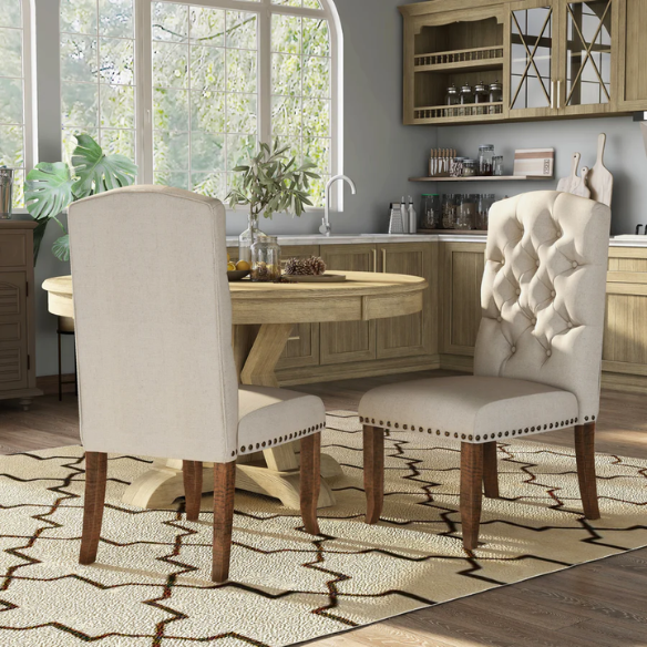 Set of 2 beige button-tufted farmhouse dining chairs with rustic wood legs, nailhead trim, and upholstered linen-like fabric.