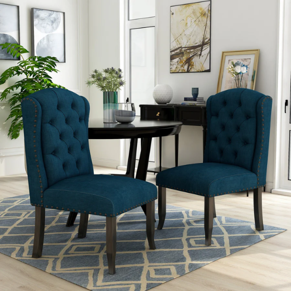 Set of two dark blue upholstered farmhouse dining chairs with tufted backs, brass nailhead trim, and antique black wood legs.