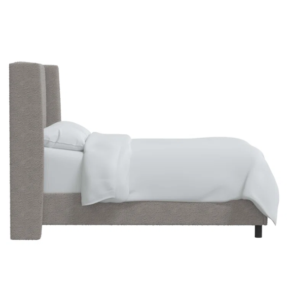 Light grey king-size upholstered bed in bouclé fabric with wingback headboard and low-profile black metal legs.