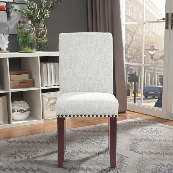Light grey upholstered Parsons chair with scrolled high back, antique bronze nailhead trim, and solid wood legs