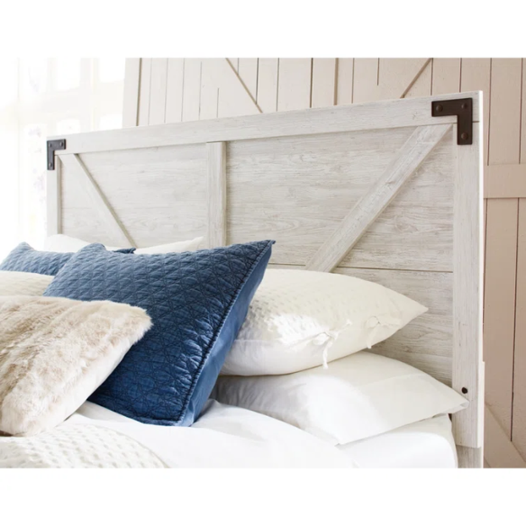 Rustic white platform bed with a distressed finish, crossbuck headboard, and metal support slats, styled in a cozy farmhouse bedroom.