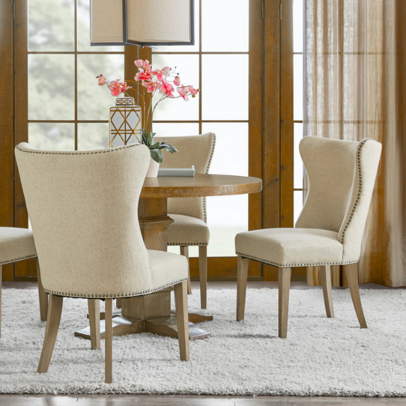 Set of two cream upholstered dining chairs with curved wingback design, dark pewter nailhead trim, and latte wood legs in a traditional style