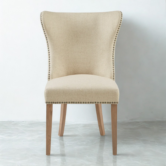 Set of two cream upholstered dining chairs with curved wingback design, dark pewter nailhead trim, and latte wood legs in a traditional style
