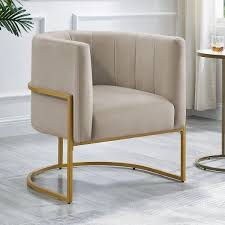 Taupe velvet barrel accent chair with gold accents and a hidden, storable ottoman. Features flared arms, foam-filled seat and back for comfort, a solid wood frame with a sled base for stability, and includes toss pillows for added comfort. The ottoman conveniently tucks under the chair to save space, creating a stylish, space-saving solution for any room.
