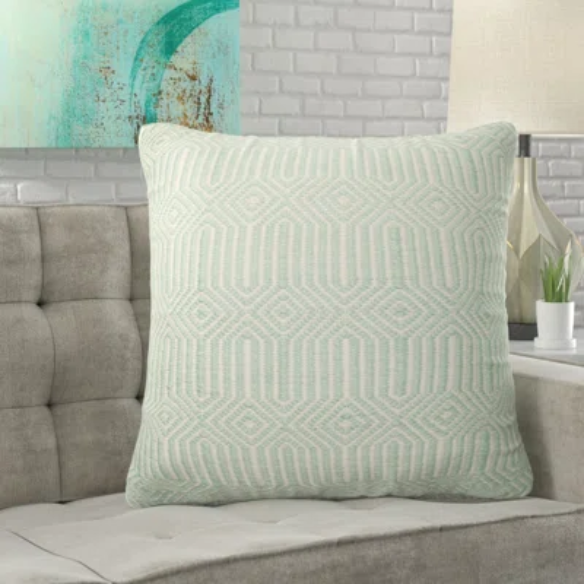 Seafoam green and cream geometric throw pillow on an outdoor patio chair with modern decor