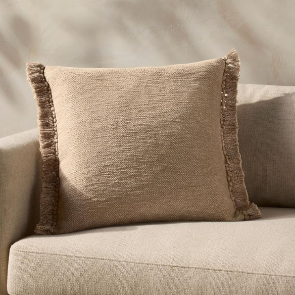 Tan cotton blend throw pillow with fringe, 22x22 square cushion featuring soft texture and hidden zipper, styled on a neutral sofa for cozy, earthy decor.